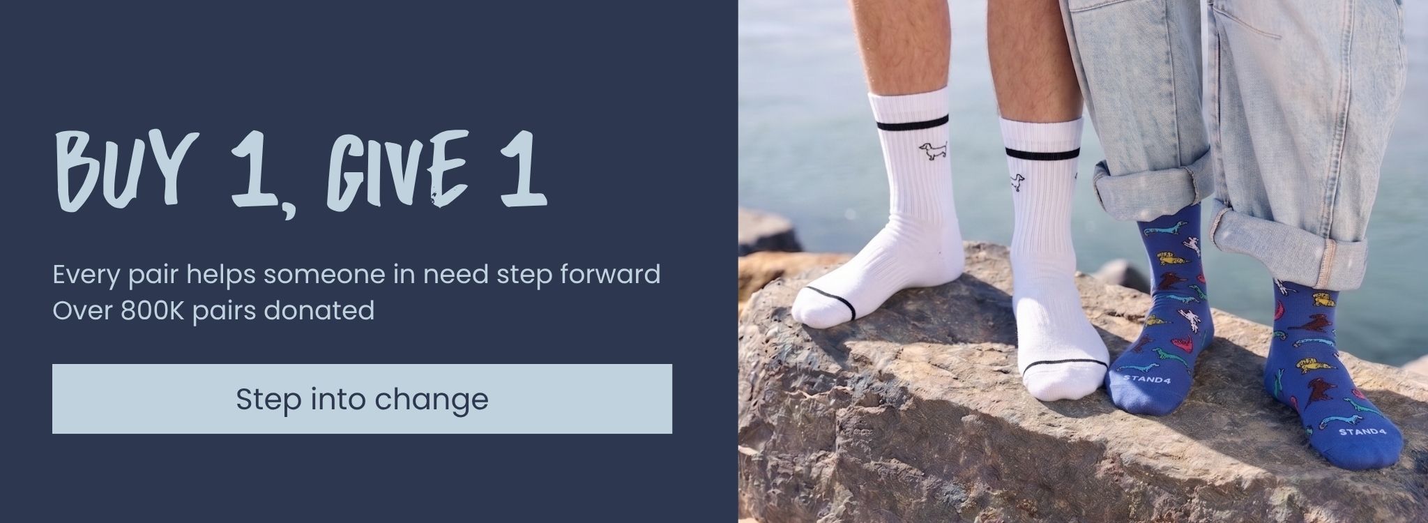 Two pairs of socks, one white and one blue with red patterns, worn by a person standing on a rock by the water.